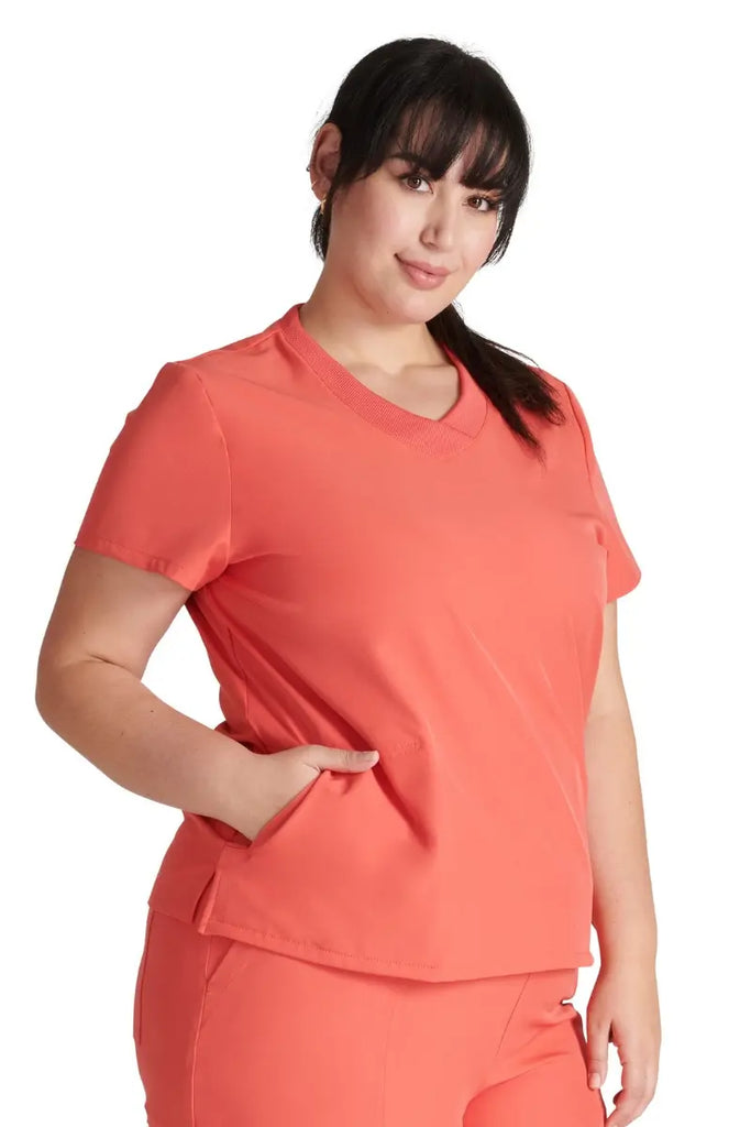 A young female Healthcare Professional wearing am Allura Women's V-neck Scrub Top in Cayenne featuring two angled front pockets.