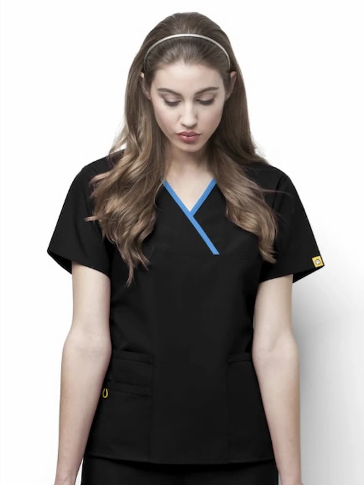A young female Licensed Practical Nurse wearing a WonderWink Origins Women's Charlie Y-neck Scrub Top in Black size XXS featuring a stylish mock wrap neckline and 5 total pockets.