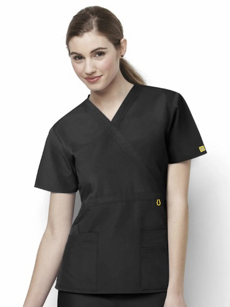 A young female Licensed Practical Nurse wearing a WonderWink Origins Women's Fashion Waist Scrub Top in Black size Medium featuring a total of 4 pockets.
