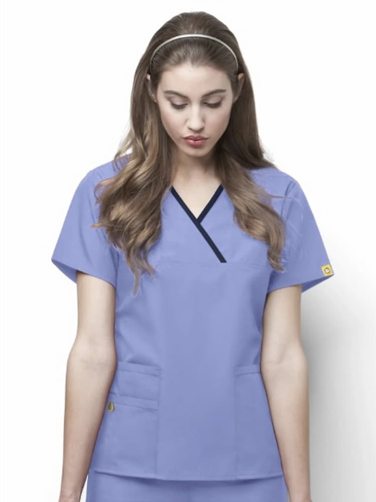 A young female Dental Hygienist wearing a WonderWink Origins Women's Y-neck Scrub Top in Ceil size 3XL featuring short sleeves and a total of 5 pockets. 