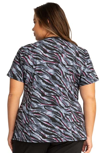 A young female CNA wearing a Cherokee Infinity Women's Mock Wrap Print Top in "Wild for Tie Dye" featuring front & back princess seams.