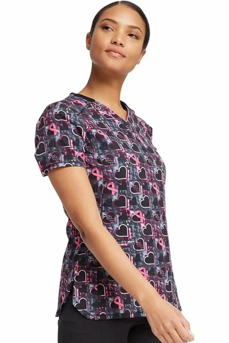 A female CNA wearing a Cherokee Infinity Women's Print V-neck Scrub Top in "Caring Beats" featuring front  and back shoulder yokes for additional shaping.