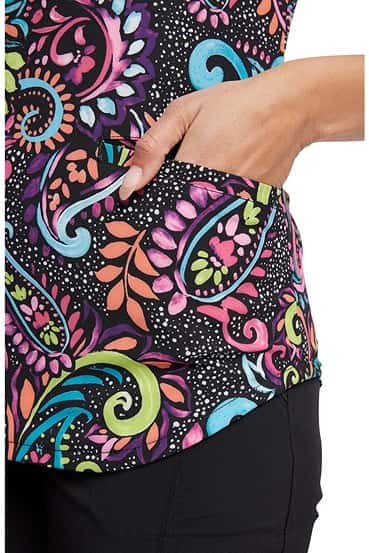 A female Healthcare Professional wearing a Cherokee Women's V-Neck Print Scrub Top in "Painted Paisley" featuring 2 front angled welt pockets.
