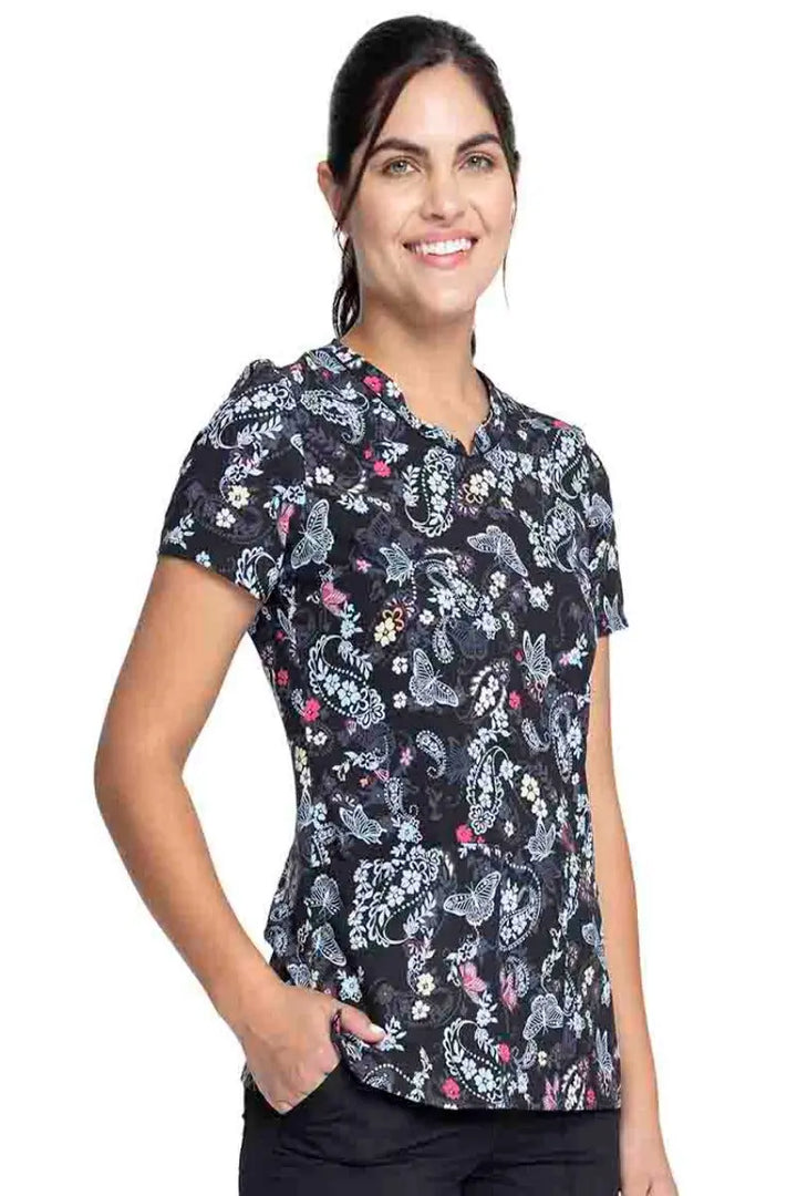 Female nurse wearing a Cherokee Women's V-Neck Print Top in "Flutter Blooms" featuring side vents for additional range of motion.