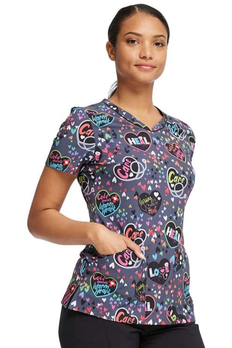 A female Home Care Registered Nurse wearing a Cherokee Women's V-Neck Print Top in "Work of Heart" featuring 2 front patch pockets.