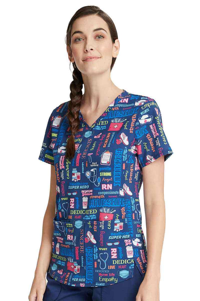 Young woman wearing a Cherokee Women's V-Neck Print Top in "Scrub Life" featuring front princess seaming to ensure a flattering all day fit.