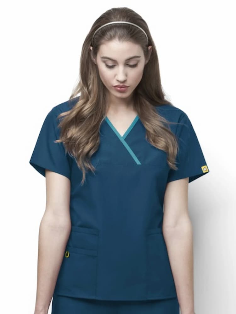 A middle aged female Dental Assistant wearing a WonderWink Women's Charlie Y-neck Scrub Top in Caribbean size 2XL featuring a total of 5 pockets.