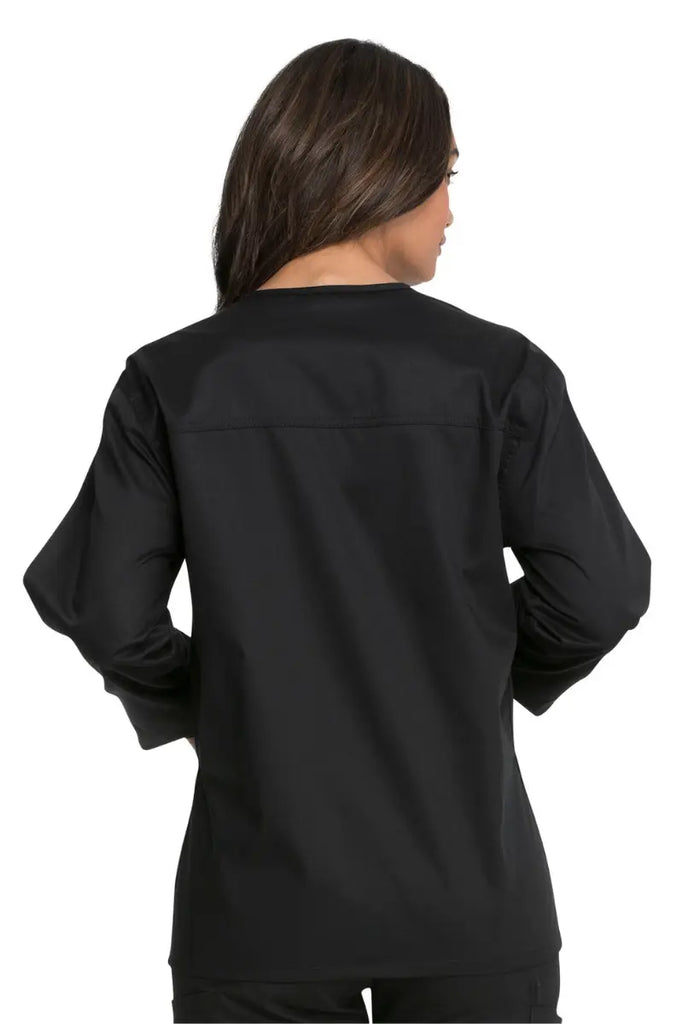 A young female CNA showcasing the back of the Dickies Industrial Unisex Warm-Up Scrub Jacket in Black featuring a center back length of 29".