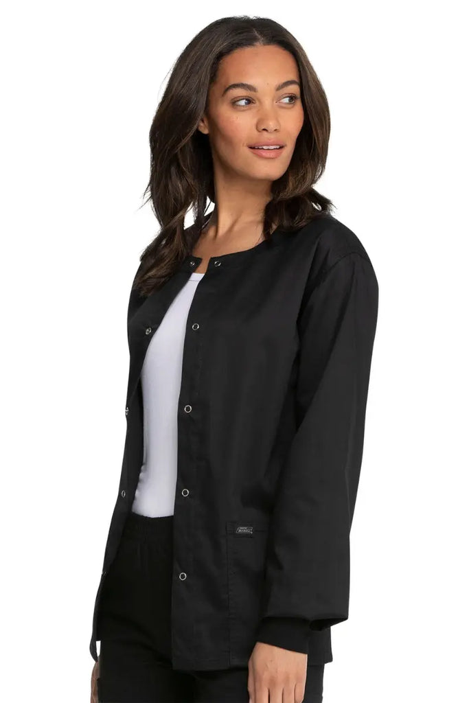 A young female Nurse wearing a Dickies Industrial Unisex Warm-Up Scrub Jacket in Black size Medium featuring a durable 80% polyester / 20% cotton stretch twill that can withstand daily wear and washing demands.