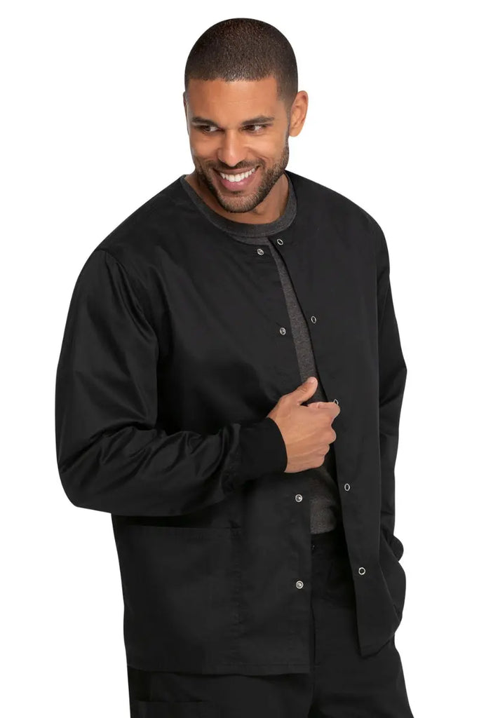 A young male Trauma Coordinator wearing a Dickies Industrial Unisex Warm-Up Scrub Jacket in Black featuring two large front patch pockets.