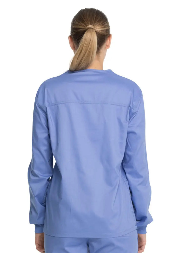 A young female Dental Assistant showcasing the back of the Dickies Industrial Unisex Warm-Up Scrub Jacket in Ceil Blue featuring a center back length of 29".