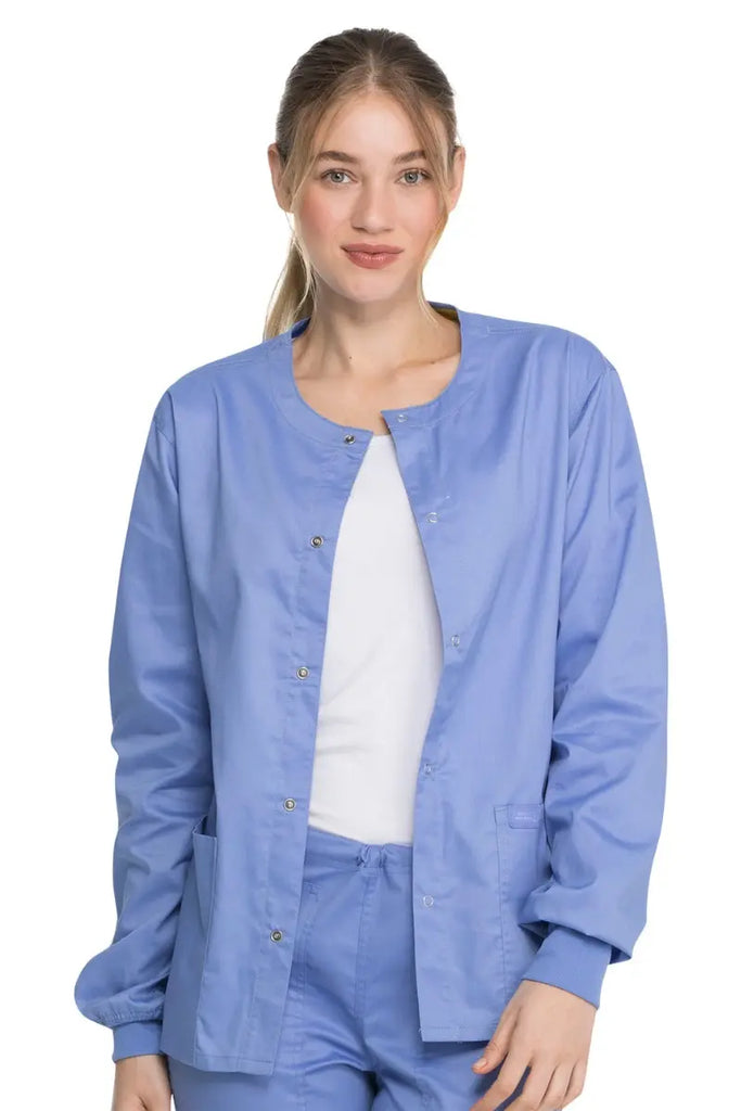 A young female Dental Hygienist wearing a Dickies Industrial Unisex Warm-Up Jacket in Ceil Blue size XXS featuring a 5 metal button closure.