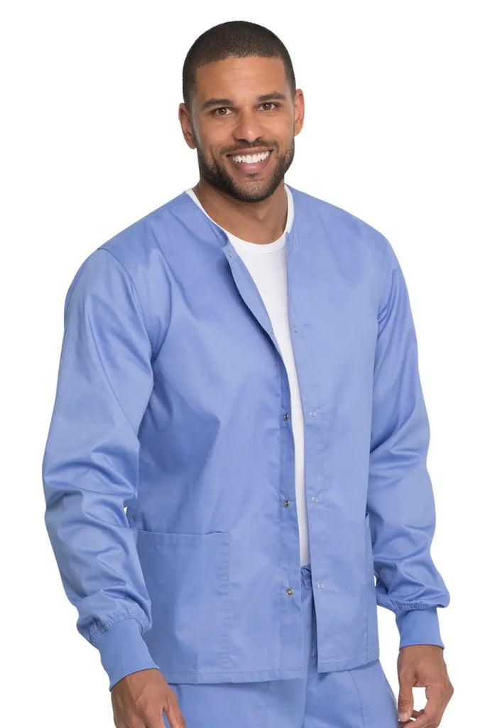 A young male MD wearing a Dickies Industrial Unisex Warm-Up Scrub Jacket in Ceil Blue featuring two large front patch pockets.