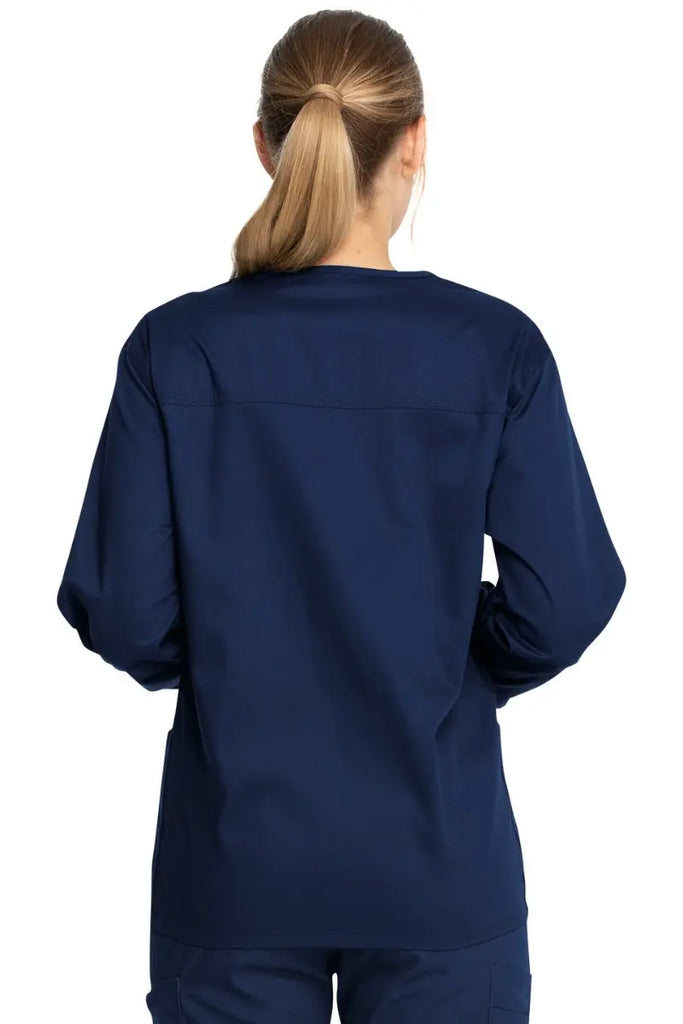 A young female Certified Nursing Assistant showcasing the back of the Dickies Industrial Unisex Warm-Up Scrub Jacket in Navy Blue featuring a center back length of 29".