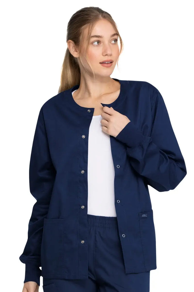 A young female Nurse Practitioner wearing a Dickies Industrial Unisex Warm-Up Jacket in Navy Blue size XS featuring a 5 metal button closure.