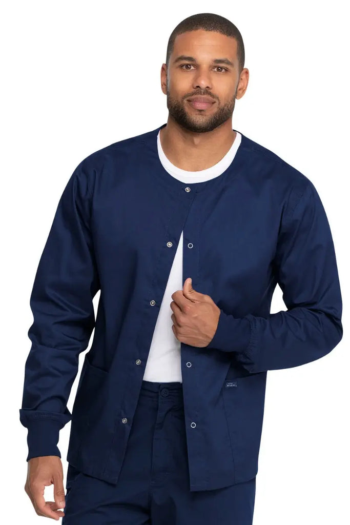 A young male Nurse wearing a Dickies Industrial Unisex Warm-Up Jacket in Navy Blue size 3XL featuring an easy care fabric made to withstand industrial laundering.