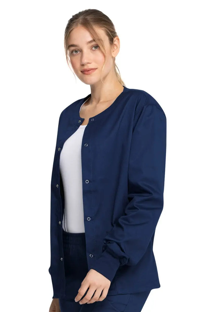 A young female Doctor wearing a Dickies Industrial Unisex Warm-Up Scrub Jacket in Navy Blue size Large featuring a durable 80% polyester / 20% cotton stretch twill that can withstand daily wear and washing demands.