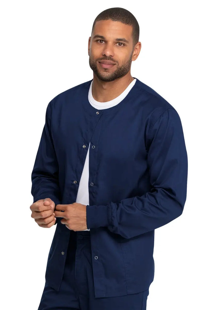 A young male Nursing Student wearing a Dickies Industrial Unisex Warm-Up Scrub Jacket in Navy Blue featuring a rib knit hem for a snug and comfortable fit that keeps out drafts.