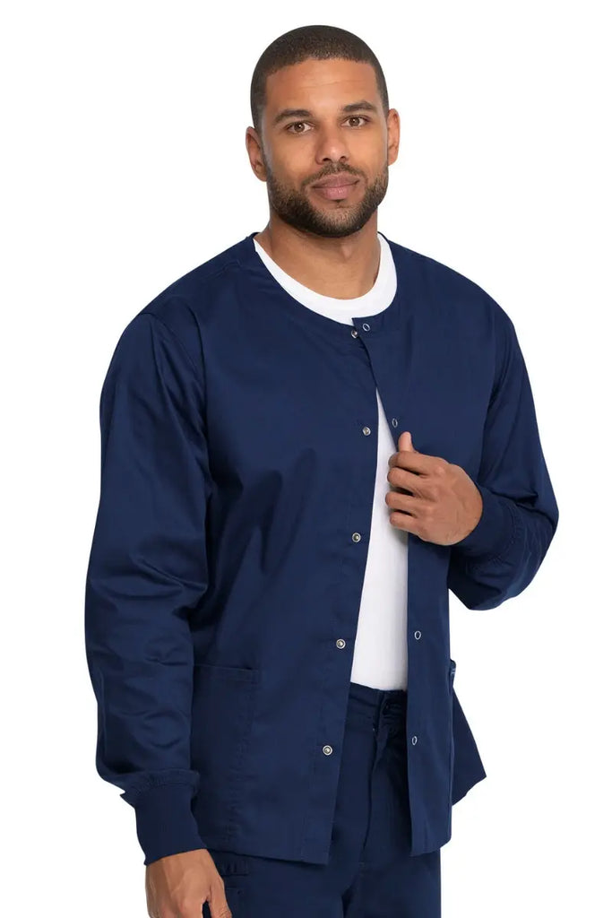 A young male Nurse Practitioner wearing a Dickies Industrial Unisex Warm-Up Scrub Jacket in Navy Blue featuring two large front patch pockets.