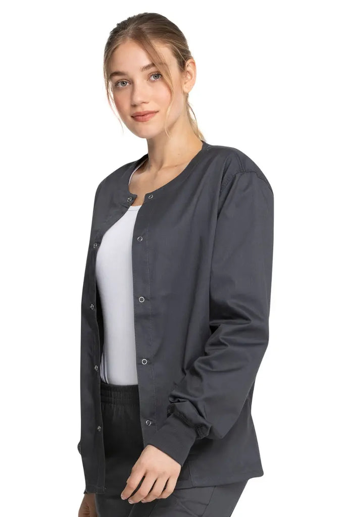 A young female Licensed Practical Nurse wearing a Dickies Industrial Unisex Warm-Up Scrub Jacket in Pewter featuring a durable 80% polyester / 20% cotton stretch twill that can withstand daily wear and washing demands.