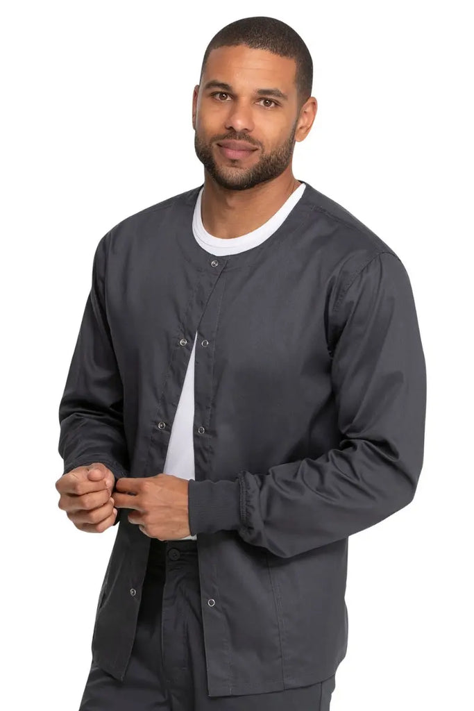 A young male Medical Receptionist wearing a Dickies Industrial Unisex Warm-Up Scrub Jacket in Pewter featuring a rib knit hem for a snug and comfortable fit that keeps out drafts.