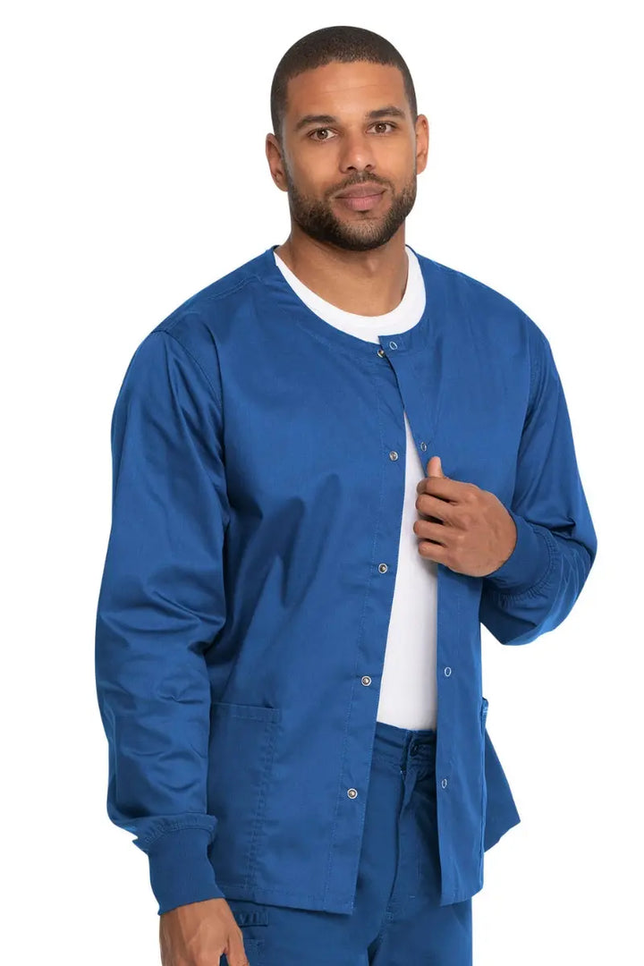 A young male Ophthalmology Medical Assistant  wearing a Dickies Industrial Unisex Warm-Up Scrub Jacket in Royal Blue featuring two large front patch pockets.