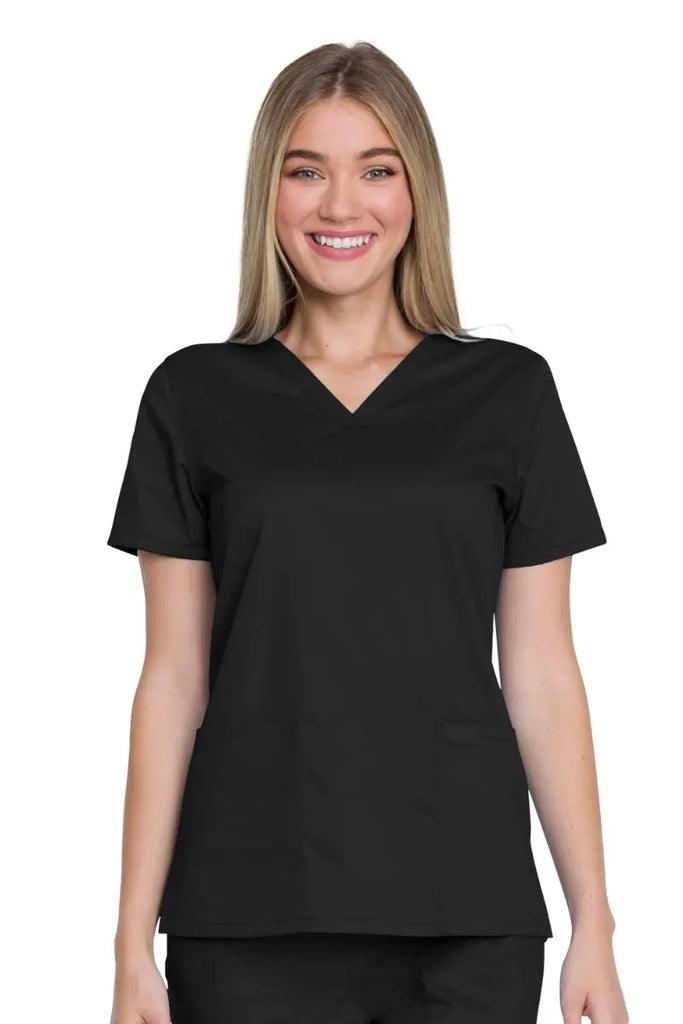 A young female Medical Specialist wearing a Dickies Industrial Women's V-Neck Scrub Top in Black size XS featuring a flattering Modern Classic Fit for a flattering silhouette designed for the female form.