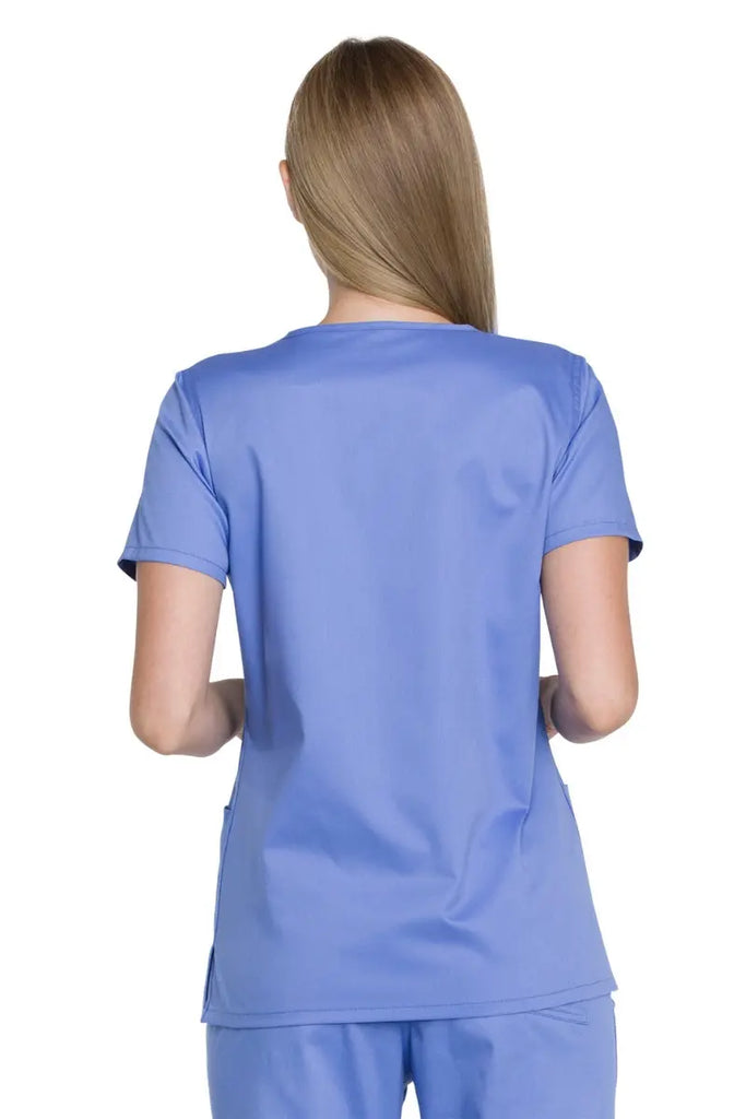 A young female Medical Student wearing a Dickies Industrial Women's V-Neck Scrub Top in Ceil Blue size Small featuring side slits for enhanced breathability and additional range of motion throughout the day.