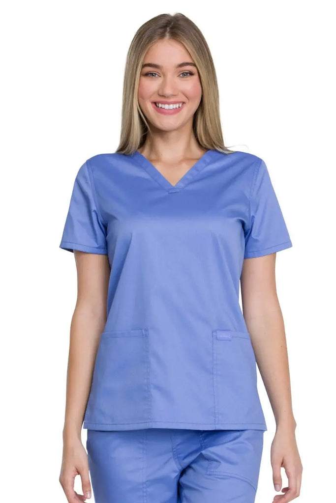 A young female Paramedic wearing a Dickies Industrial Women's V-neck Scrub Top in Ceil Blue size Large featuring two front patch pockets for ample storage space on the job.