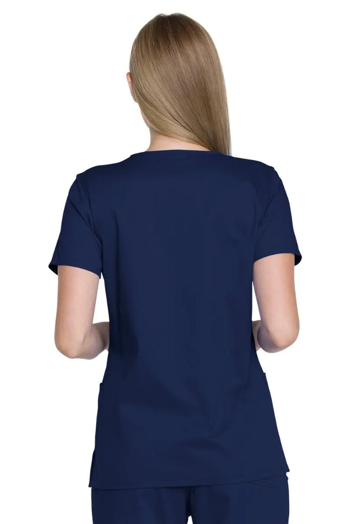A young female Physicians Assistant wearing a Dickies Industrial Women's V-Neck Scrub Top in Navy Blue size 2XL featuring a wrinkle-resistant fabric that minimizes the need for ironing.