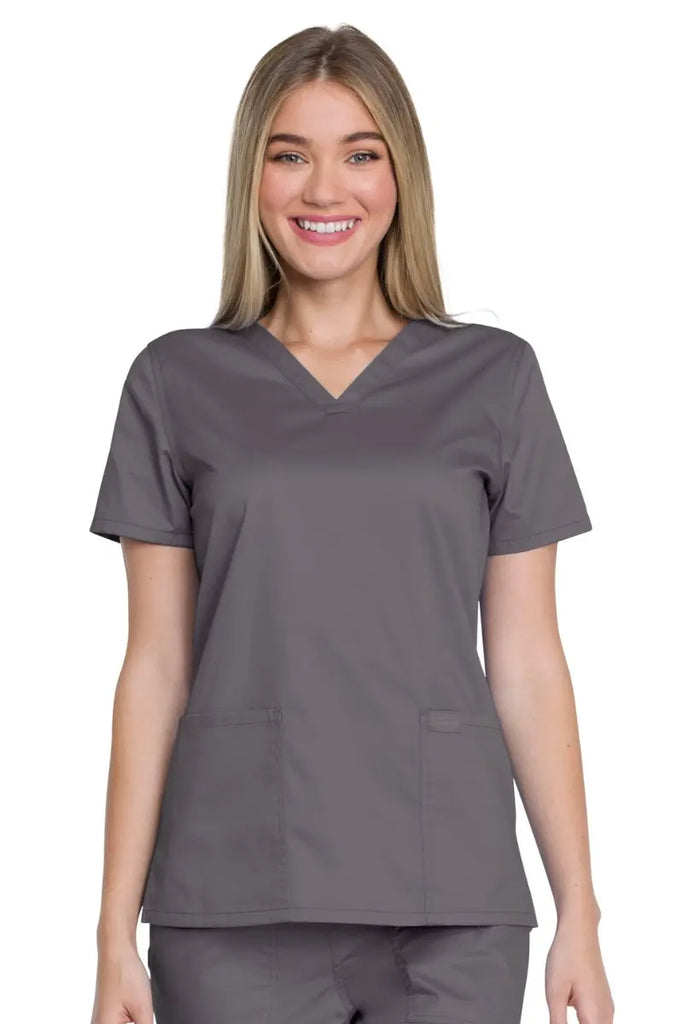 A young female Pharmacy Technician wearing a Dickies Industrial Women's V-Neck Scrub Top in Pewter featuring two front patch pockets and a hidden side seam pocket for all of your on the go storage needs.