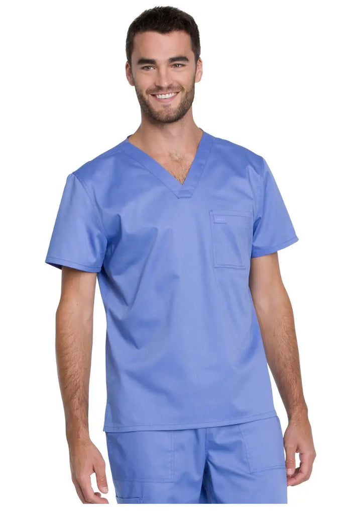A young male Medical Student wearing a Dickies Industrial Unisex Tuckable V-Neck Scrub Top in Ceil Blue size 3XL made from a durable 80/20 polyester-cotton stretch twill blend.