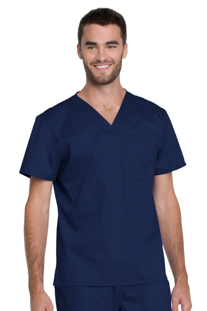 A young Male Nurse wearing a Dickies Industrial Unisex Tuckable V-Neck Scrub Top in Navy Blue featuring a unique construction made from easy-care materials that wash clean while maintaining their shape.