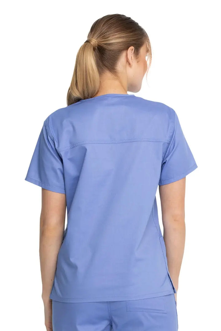 A young female Dental Hygienist showcasing the back of the Dickies Industrial Unisex V-Neck Scrub Top in Ceil Blue size Small featuring bartacks at stress points to provide extra strength and prevent tearing.