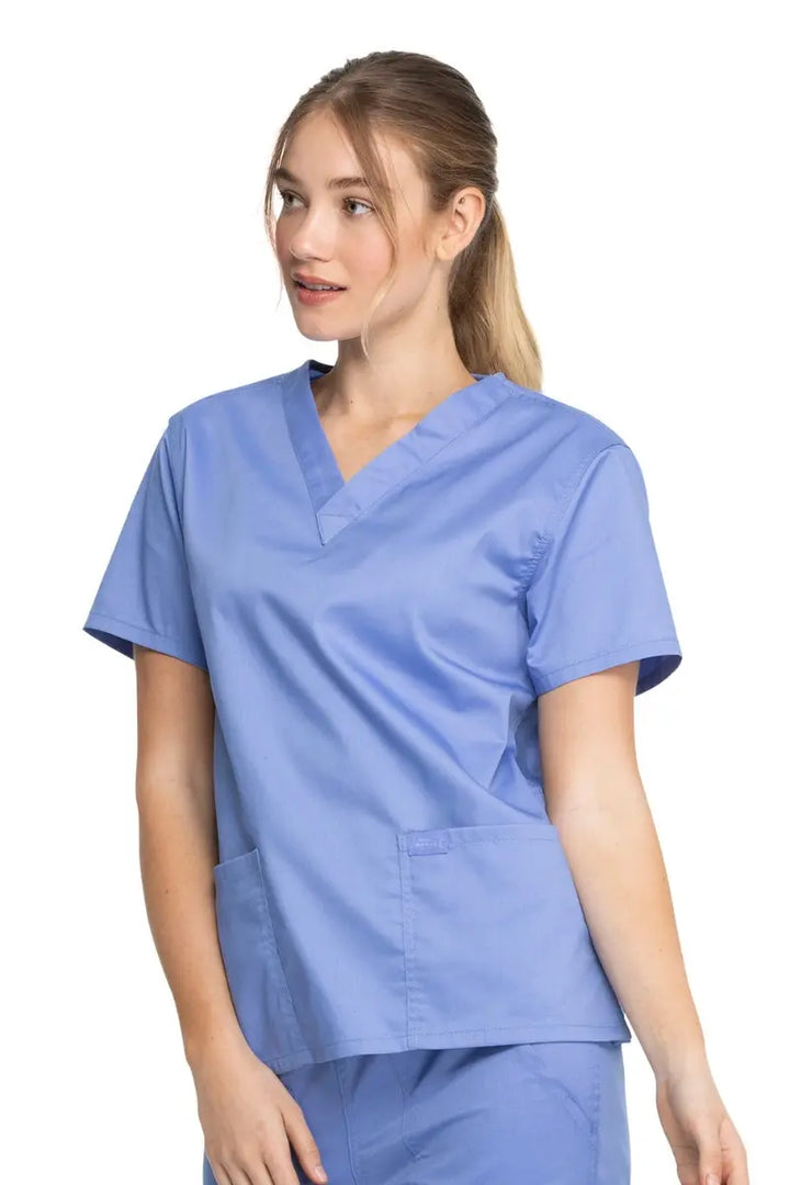 A young female Nurse wearing a Dickies Industrial Unisex V-Neck Scrub Top in Ceil Blue size Medium featuring side slits for enhanced breathability and additional range of motion throughout the day.