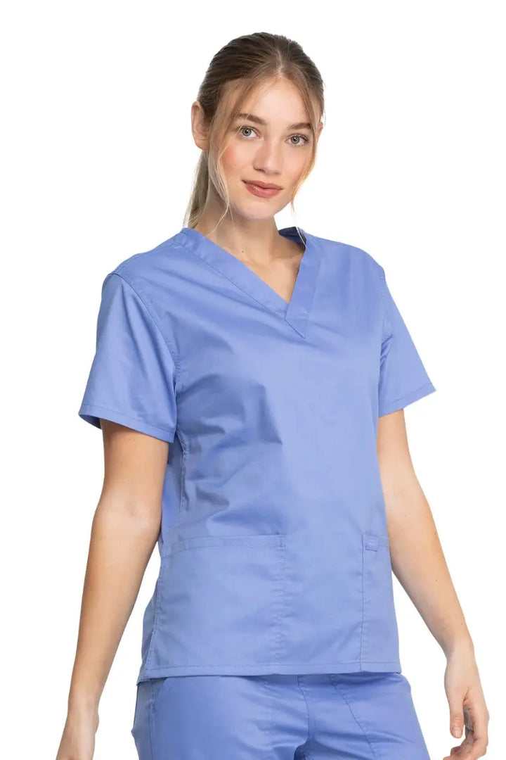 A young female Dental Assistant wearing a Dickies Industrial Unisex V-Neck Scrub Top in Ceil Blue size XXS featuring short sleeves.