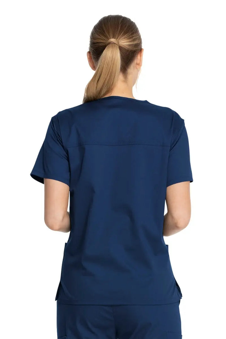 A young female LVN showcasing the back of the Dickies Industrial Unisex V-Neck Scrub Top in Navy Blue size Small featuring bartacks at stress points to provide extra strength and prevent tearing.