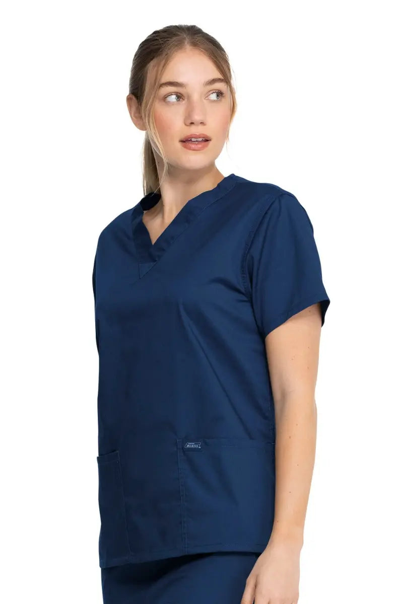 A young female CRNA wearing a Dickies Industrial Unisex V-Neck Scrub Top in Navy Blue size Medium featuring side slits for enhanced breathability and additional range of motion throughout the day.