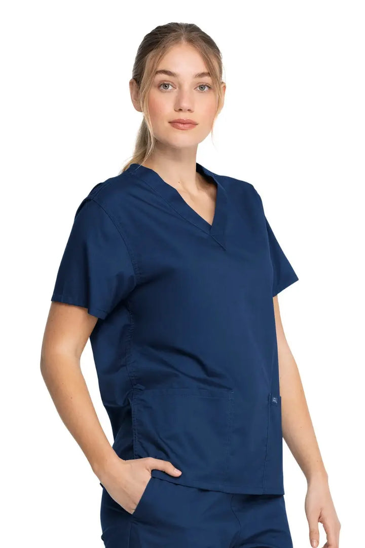 A young female Registered Nurse wearing a Dickies Industrial Unisex V-Neck Scrub Top in Navy Blue size XS featuring a flattering fit that ensures a comfortable and professional fit for men and women.