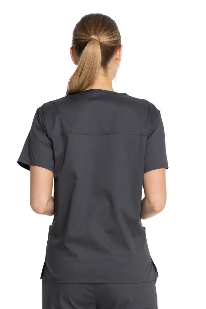 A young female Sonographer showcasing the back of the Dickies Industrial Unisex V-Neck Scrub Top in Pewter size Small featuring bartacks at stress points to provide extra strength and prevent tearing.