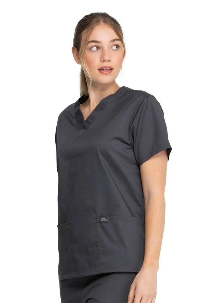 A young female Cardiovascular Technologist wearing a Dickies Industrial Unisex V-Neck Scrub Top in Pewter size Medium featuring side slits for enhanced breathability and additional range of motion throughout the day.