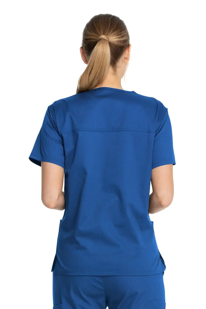 A young female Doctor showcasing the back of the Dickies Industrial Unisex V-Neck Scrub Top in Royal Blue size Small featuring bartacks at stress points to provide extra strength and prevent tearing.