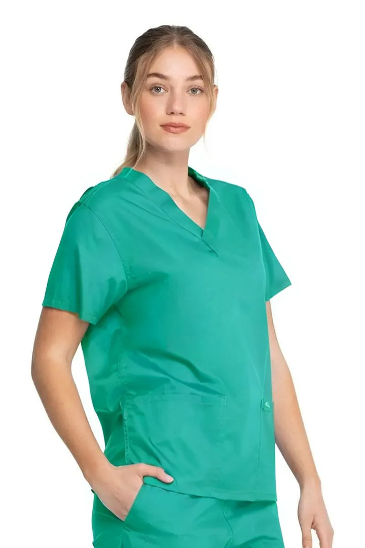 A young female Operating Room Nurse wearing a Dickies Industrial Unisex V-Neck Scrub Top in Surgical Green size Medium featuring side slits for enhanced breathability and additional range of motion throughout the day.