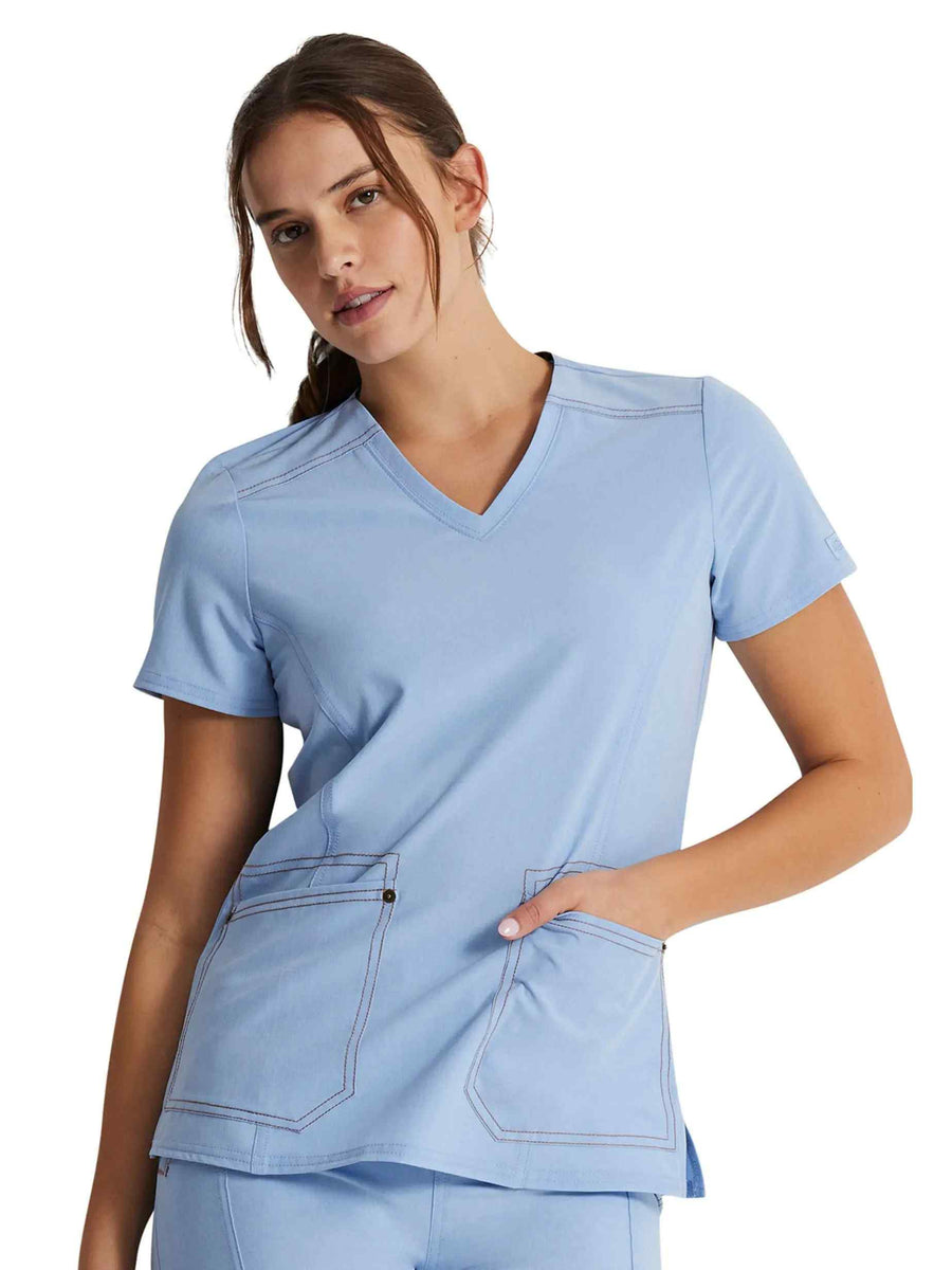 A young female Dental Assistant wearing a Dickies Riveting Women's V-neck Scrub Top in Light Chambray featuring short sleeves.