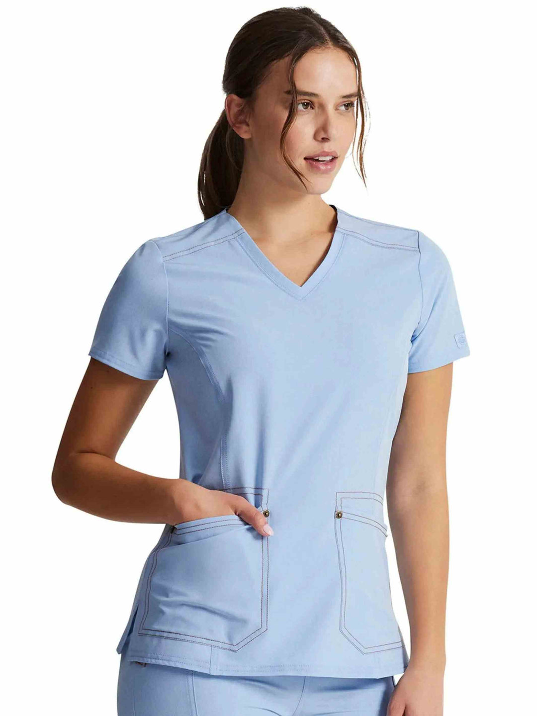 A Healthcare Professional showcasing the Dickies  Riveting Women's V-neck Scrub Top in Light Chambray size XS featuring logo rivets at the sleeves.