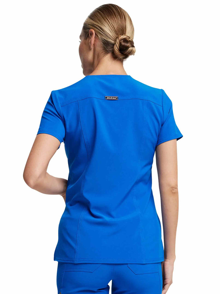 A young female nurse showcasing the back of the Dickies Riveting Women's V-neck Scrub Top in Royal Blue size medium featuring a center back length of 27.75".