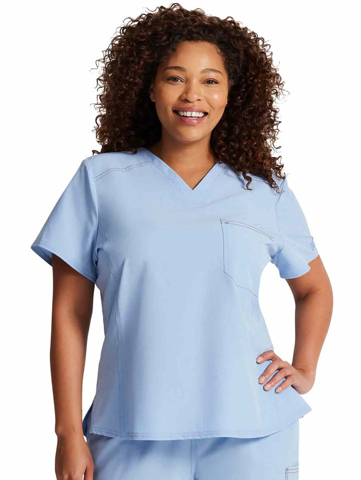 A young female Junior Nurse showcasing the front of the Dickies Riveting Women's Tuckable Scrub Top in Light Chambray featuring short sleeves.