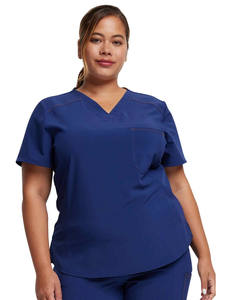 A young female LPN wearing a Dickies Riveting Women's Tuckable Scrub Top in Navy Blue featuring 1 front chest pocket.