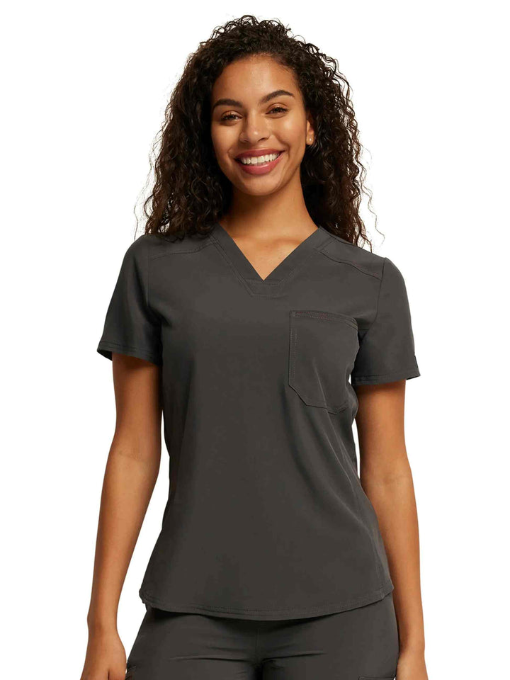 A young female Lab Tech showcasing the front of the Dickies Riveting Tuckable Scrub Top in Pewter size small featuring short sleeves.