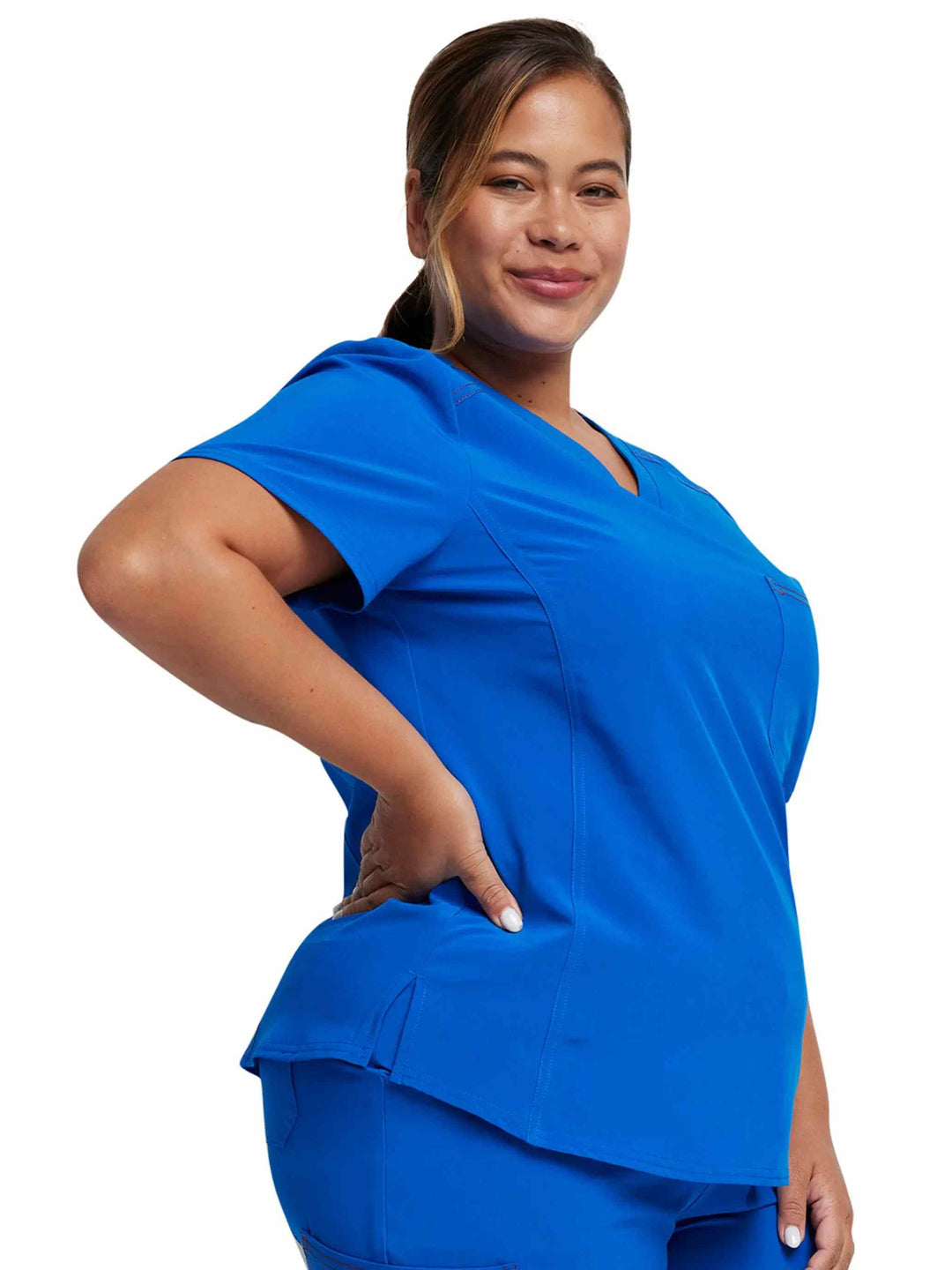 A young female Physical Therapist showcasing the side of the Dickies Riveting Women's Tuckable Scrub Top in Royal featuring side slits for additional mobility.